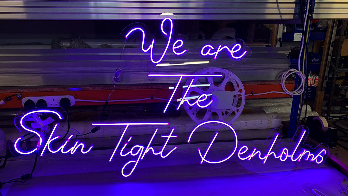 A neon sign with Denholm Associates strapline: We are the skin tight Denholms.
