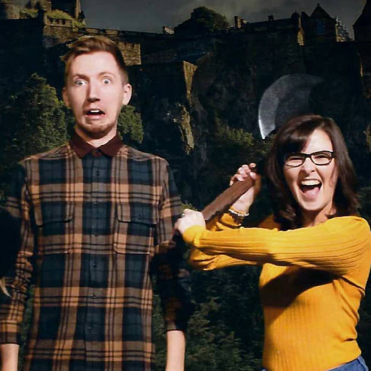 Two visitors getting their photo taken at the Edinburgh Dungeon. One is holding an axe, the other is pretending to be scared.