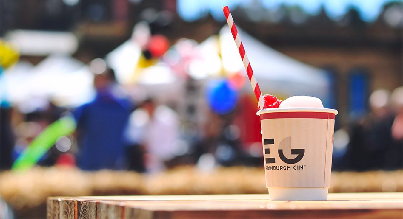 A lifestyle photo of an Edinburgh Gin ice cream cup, with a summer festival in the background.