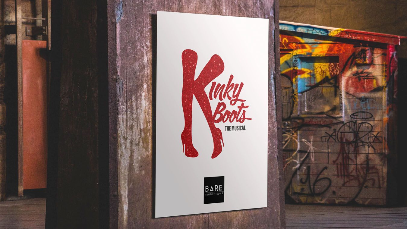 A close-up of a Kinky Boots poster in an urban scene, with Bare Productions logo on it.