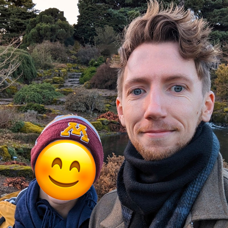 A selfie of Chris and one of his mentorship students in a botanical garden. An emoji covers the face of the student.