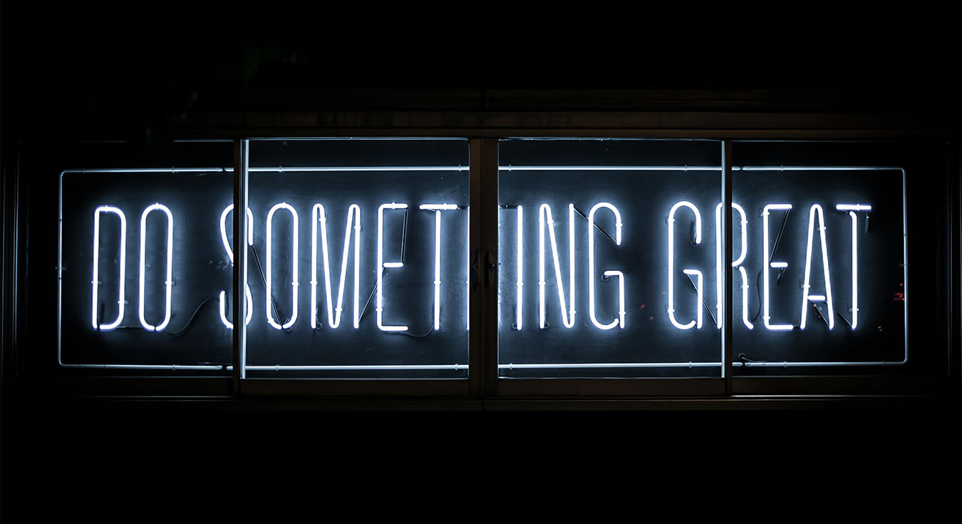 A neon sign amidst a black backdrop, saying do something great.