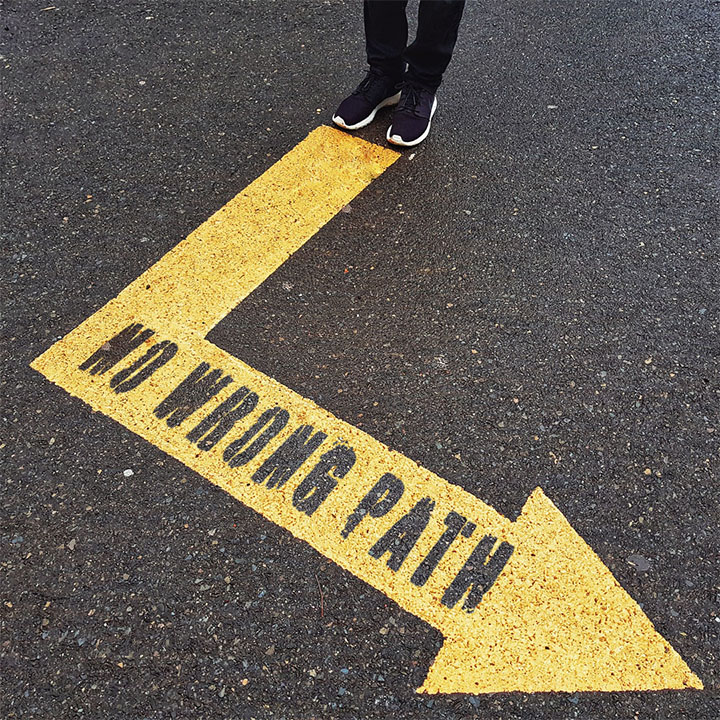 A retouched image of the same person standing on tarmac, with no wrong path edited into a bright yellow arrow.